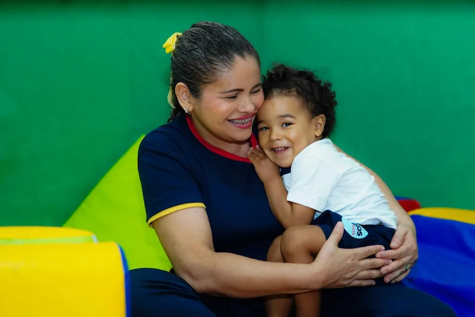 Professora abraçando uma criança e as duas sorrindo