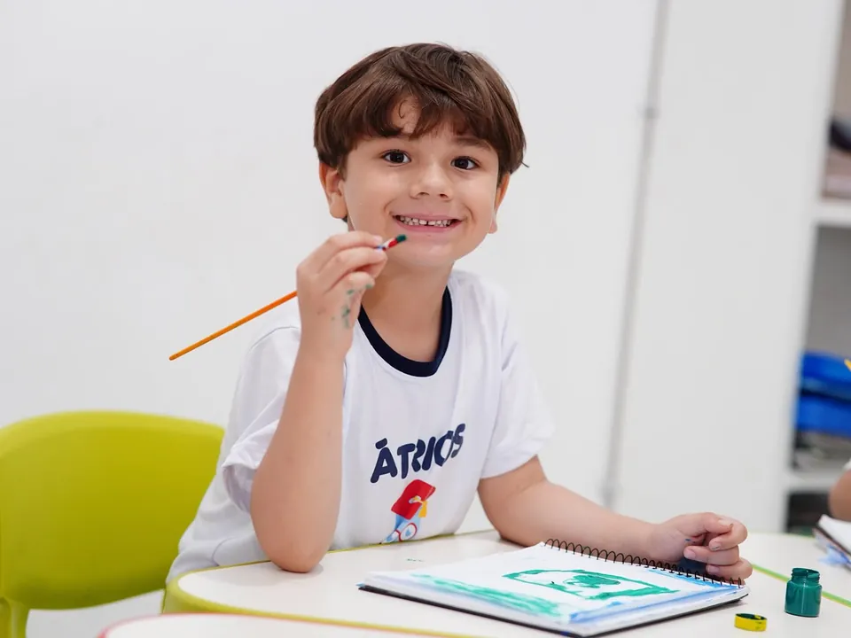 Menino pintando e sorrindo durante atividade de artes
